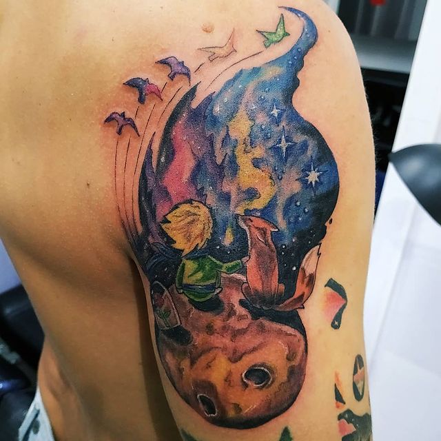 Tatuaje de El principito con el zorro sentados en su planeta. En el hombro, en color