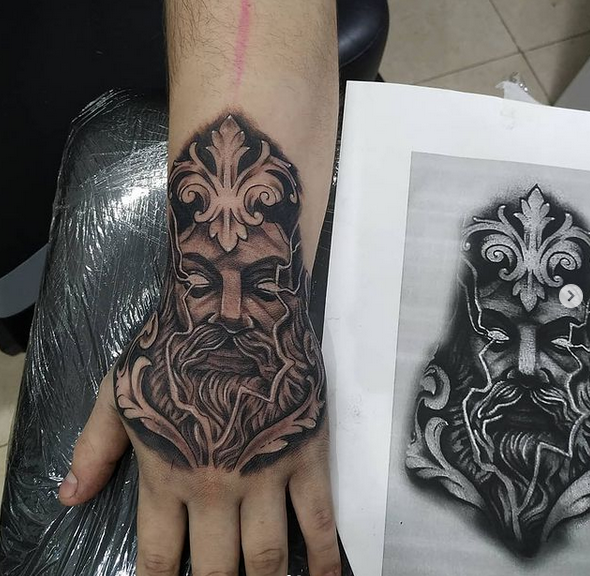 Tatuaje en la mano de la cara del dios Zeus, con adornos. En blanco y negro